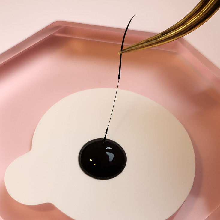 Stringy lash extension glue forming threads between tweezer and glue dot